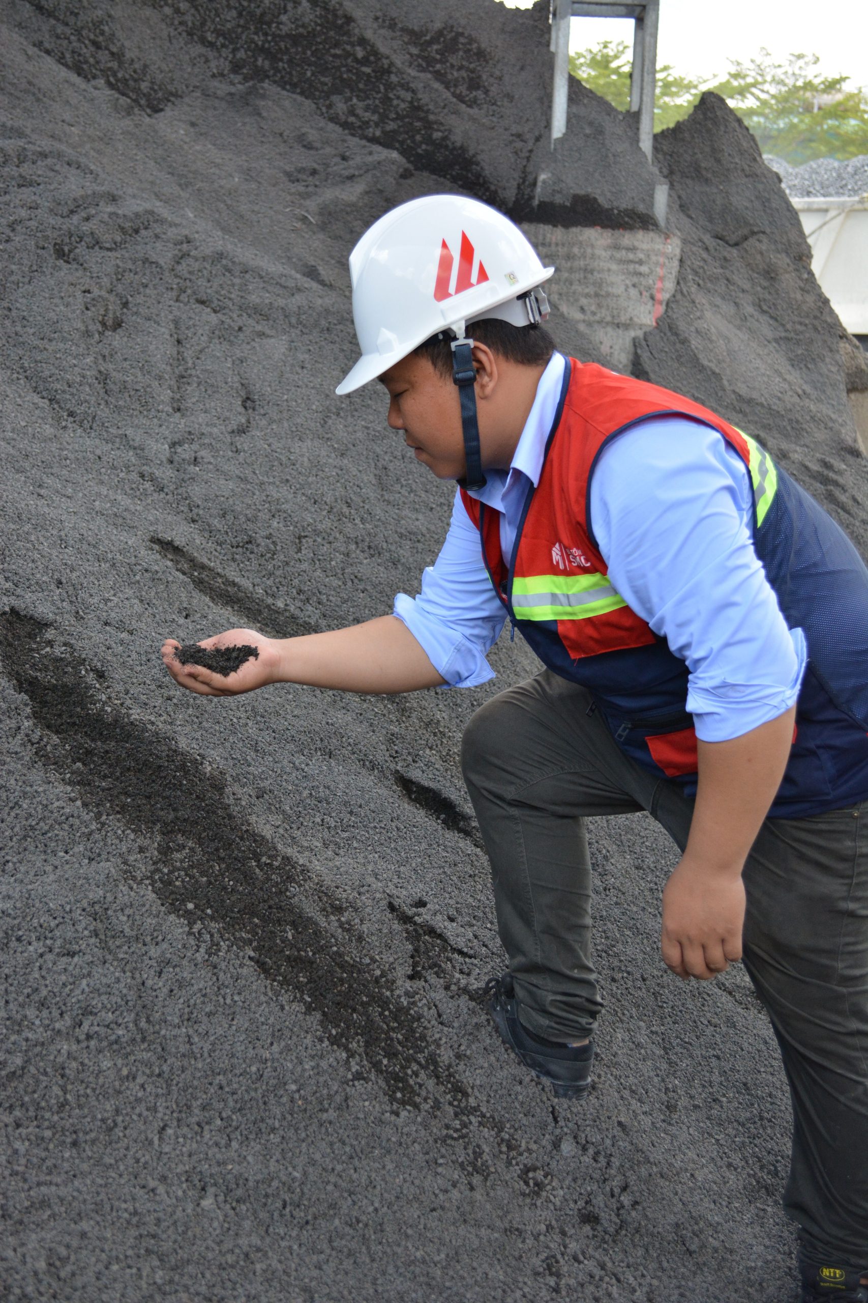 Construction worker examining a pile of material at a work site outdoors in daylight.
